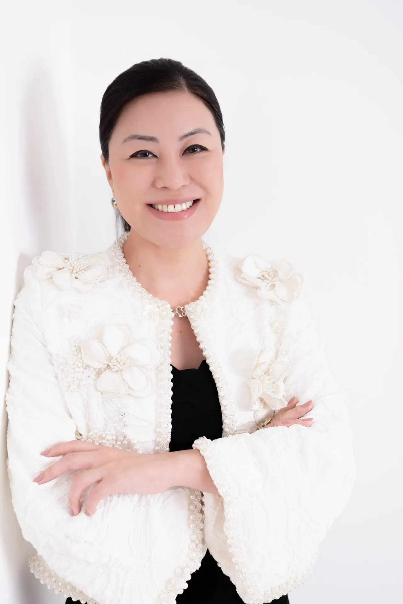 Dra. Thais Sakuma sorrindo, de braços cruzados, com casaco branco bordado